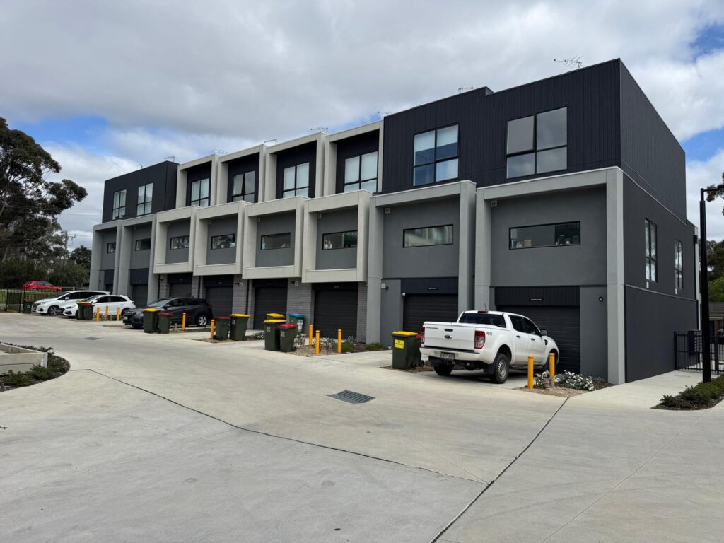 Row of townhouses with dark upper facades and light ground-floor render