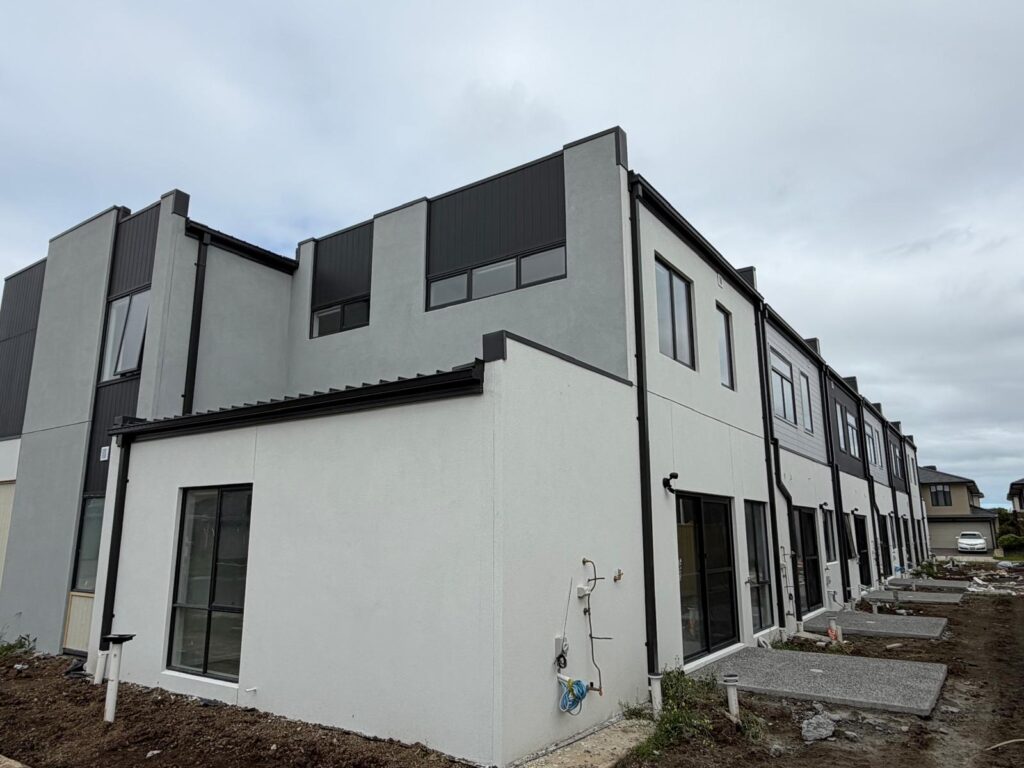 Two-storey townhouse facade with light rendered walls and dark upper panels